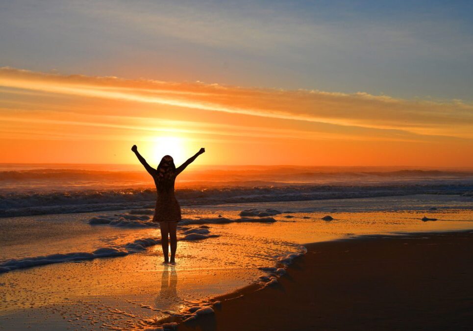 Person celebrating on beach during sunset.